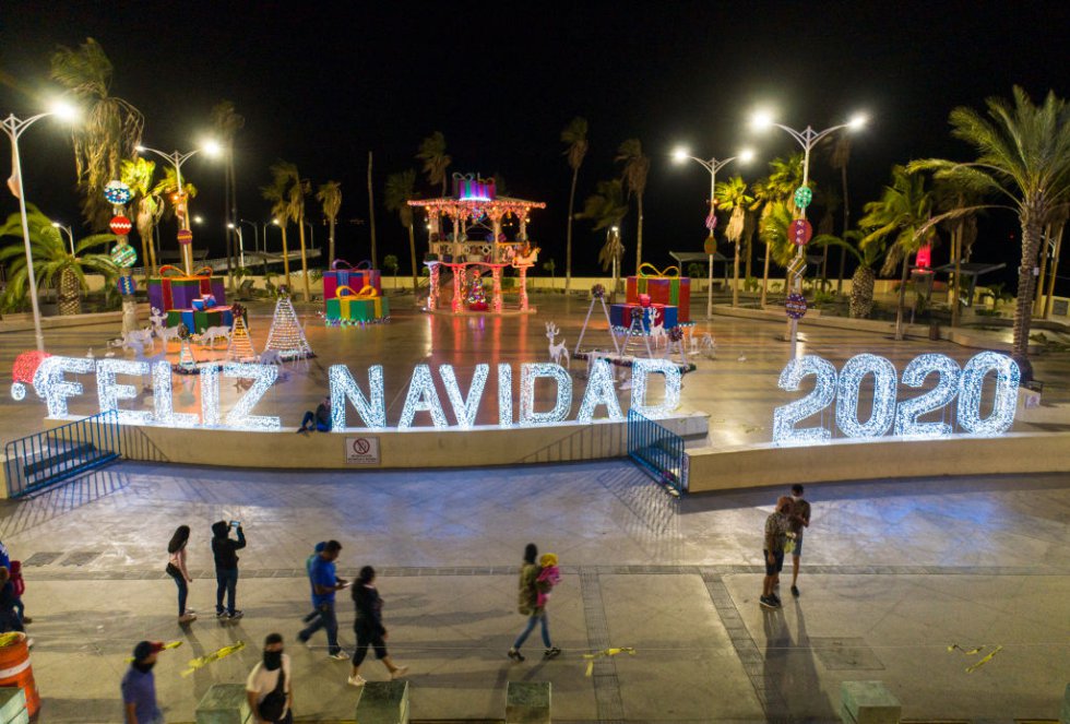La gente camina por el paseo marítimo visitando el stand decorado con un gran letrero iluminado de luces y adornos navideños de "Feliz Navidad 2020" como parte de las celebraciones de la temporada navideña el 15 de diciembre de 2020 en La Paz, México.